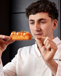 Morceau de sushi croustillant garni de saumon, crème et fines herbes, tenu par un chef en blouse blanche