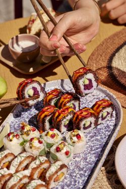 Sushi variés sur une assiette en céramique avec des baguettes prenant des pièces, cuisine japonaise colorée en extérieur.