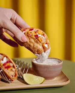 Mini tacos croustillants trempés dans une sauce blanche à côté d'un quartier de citron vert sur plateau en bois