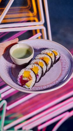Rouleaux de sushi colorés servis avec une sauce verte dans une assiette ronde au restaurant japonais Côté Sushi Genève.
