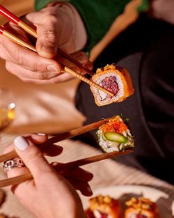 Deux personnes tenant des sushis avec des baguettes, montrant des morceaux avec différents ingrédients colorés.
