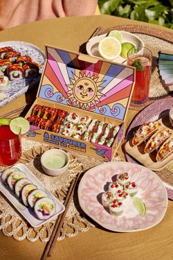 Plateaux variés de sushi à emporter avec boissons et sauces, présentés sur une table en extérieur.