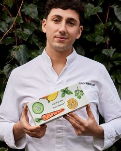 Un employé en uniforme blanc tient une boîte à sushi avec des illustrations de légumes et le nom Côté Sushi.