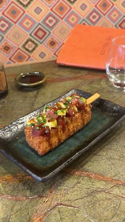 Brochette croustillante garnie de dés de poisson cru et de sauce sur une assiette foncée au restaurant Côté Sushi Genève