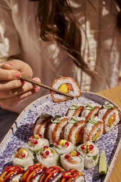 Assortiment de sushis variés sur une assiette, avec des mains tenant un sushi à l'aide de baguettes.