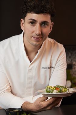 Chef portant une chemise blanche présente un plat de sushi avec concombre et saumon sur une assiette.
