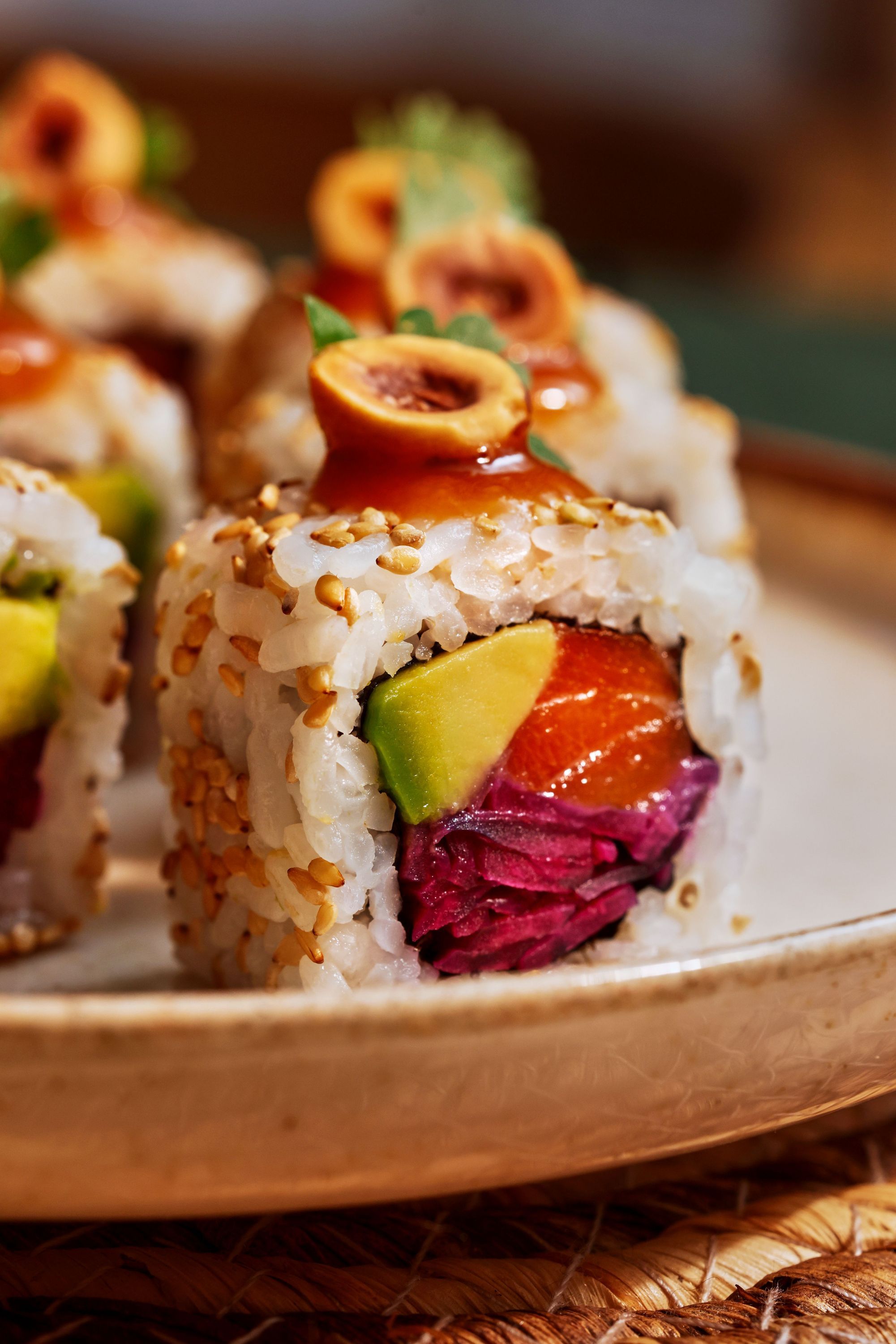 Rouleau de sushi garni de légumes frais, poisson cru, et graines de sésame, servi sur une assiette en céramique.