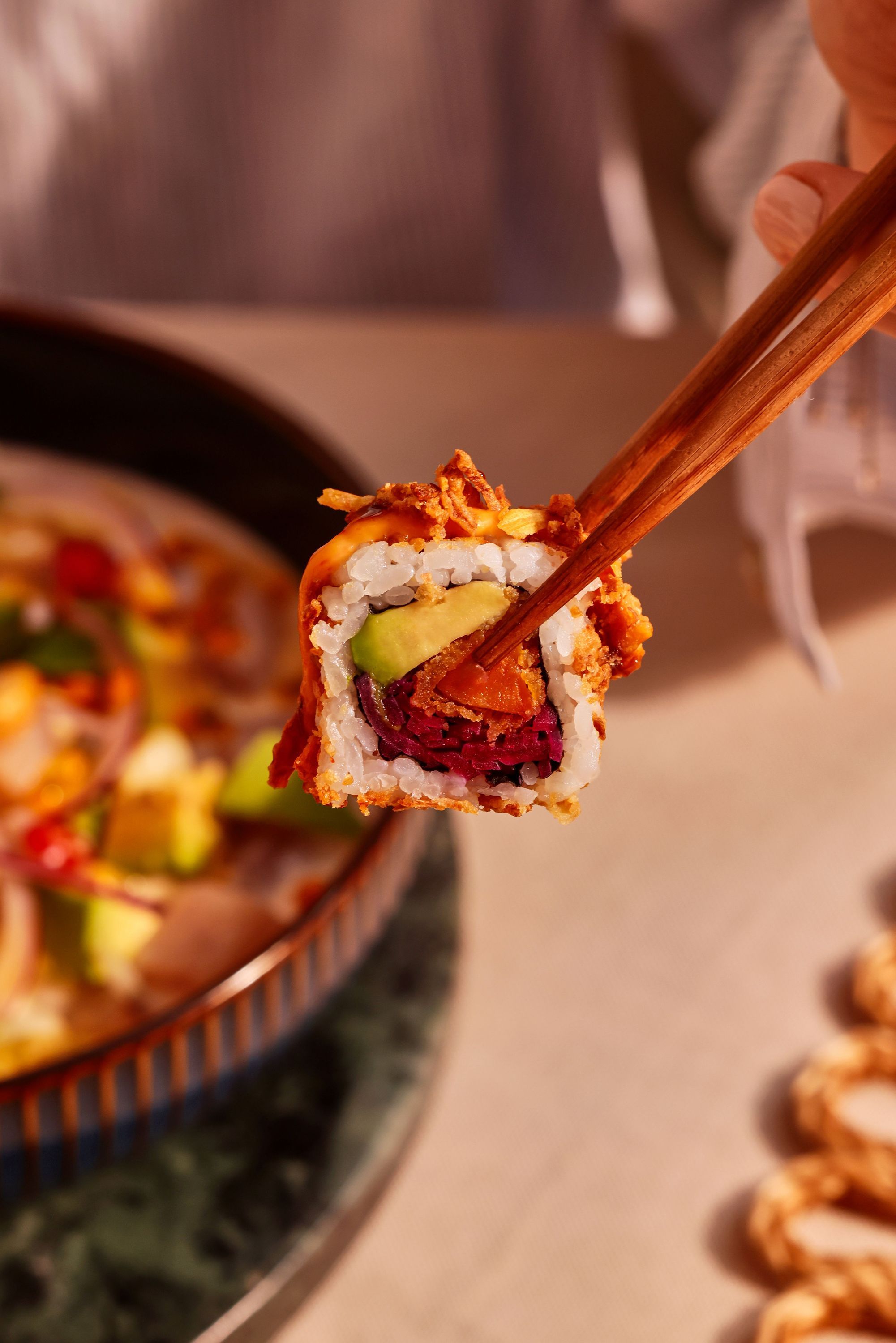 Rouleau de sushi avec avocat et légumes, tenu par des baguettes au-dessus d'une assiette floue en arrière-plan