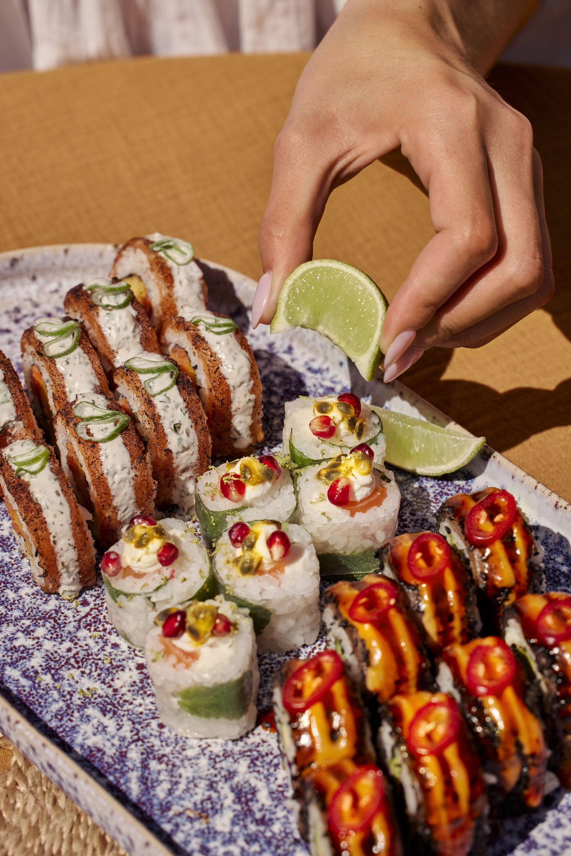 Sushi à emporter avec diverses garnitures colorées et une main pressant un quartier de citron vert.
