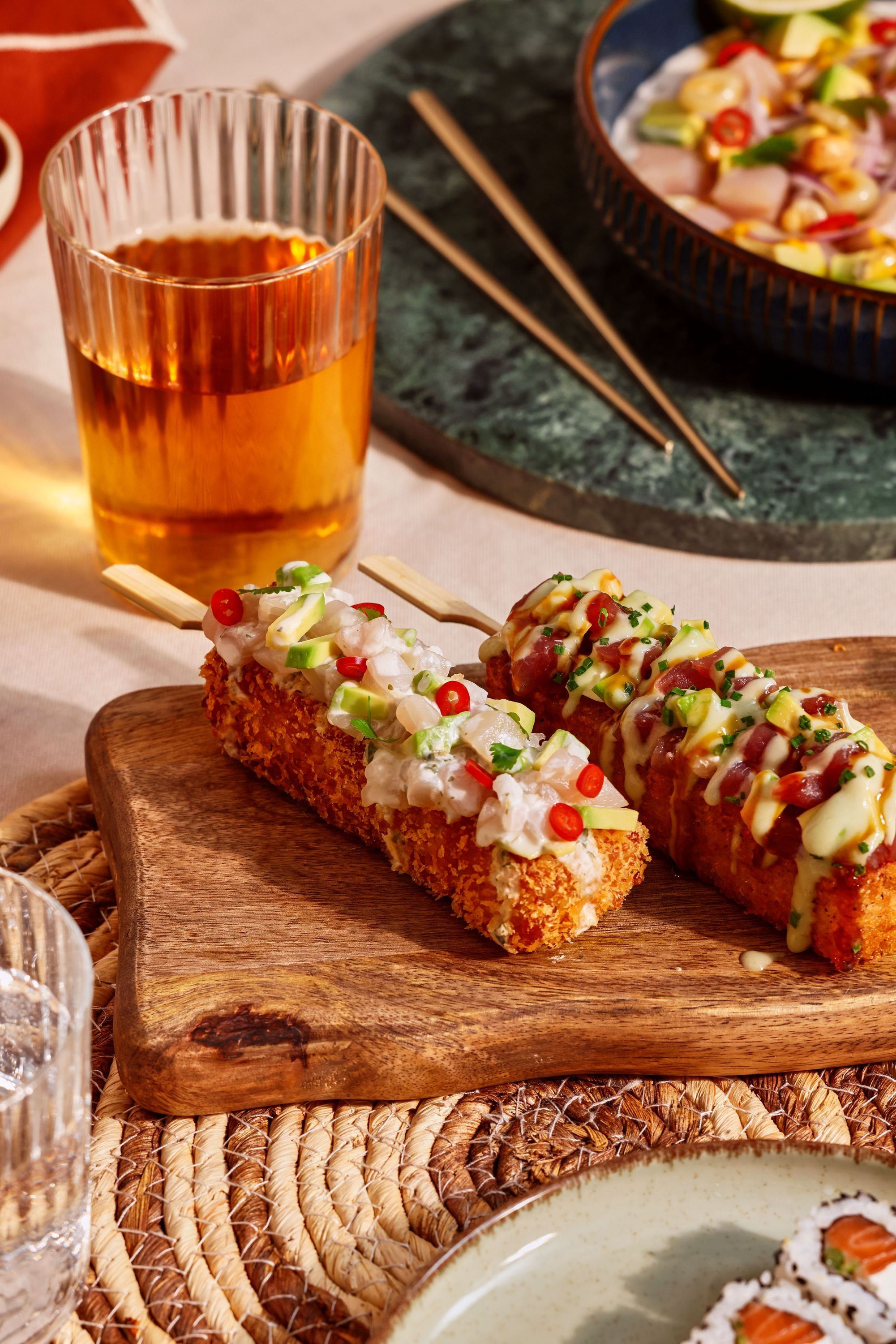 Garnitures variées sur sushi croustillant présentées sur planche en bois avec verre de boisson à côté