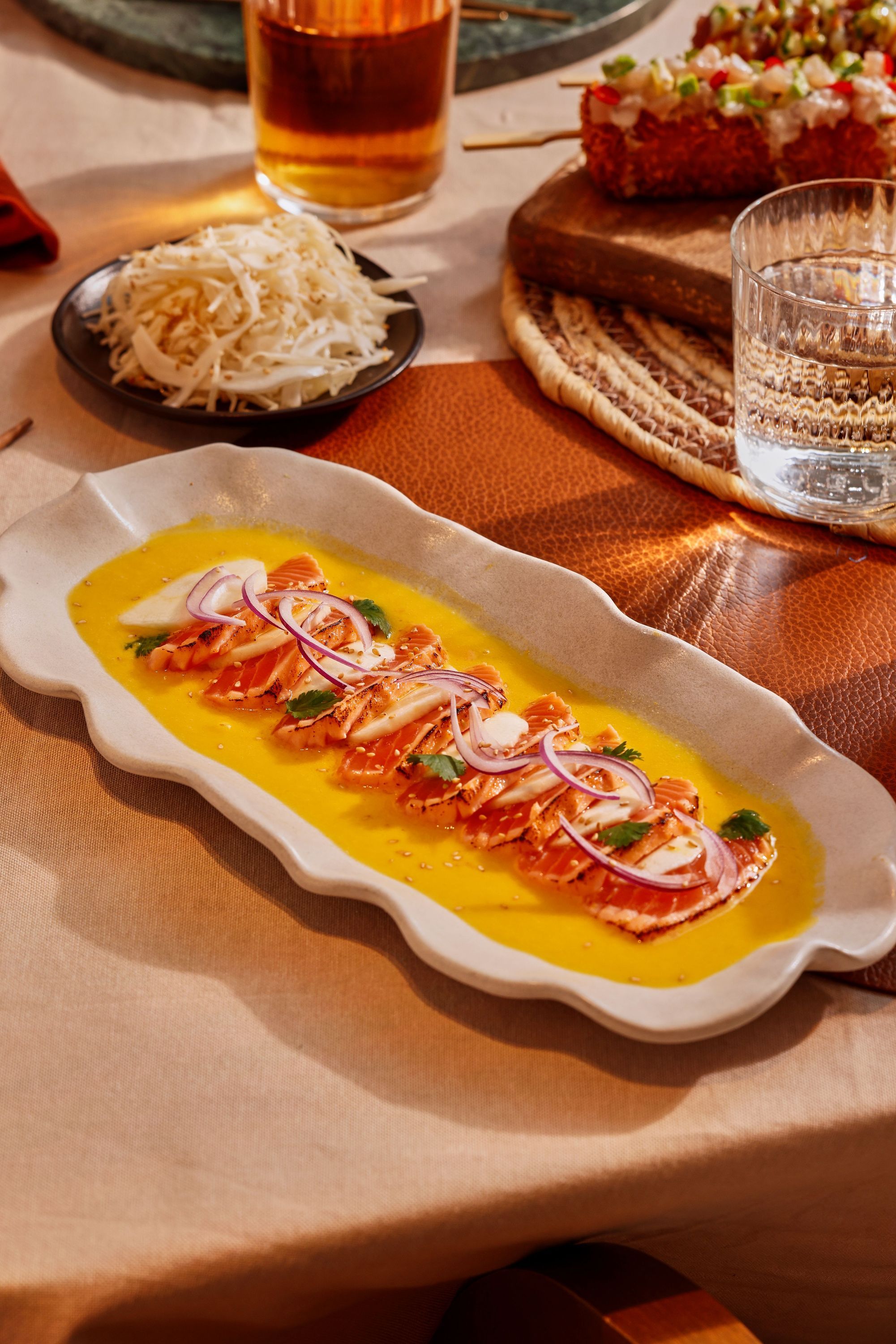 Tranches de saumon sur sauce jaune, garnies d'oignon rouge et coriandre, présentées dans un plat blanc ondulé.